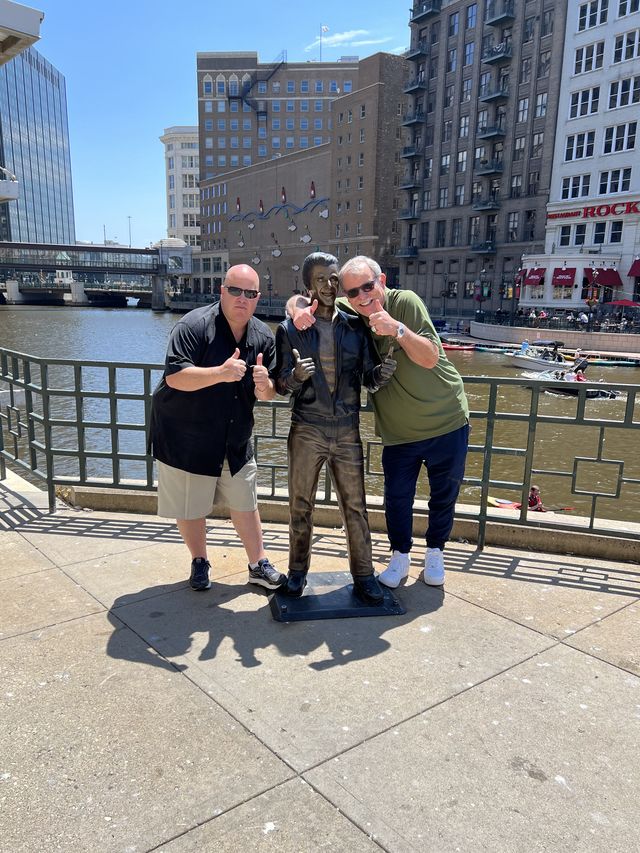 Three people posing beside a statue on a riverwalk