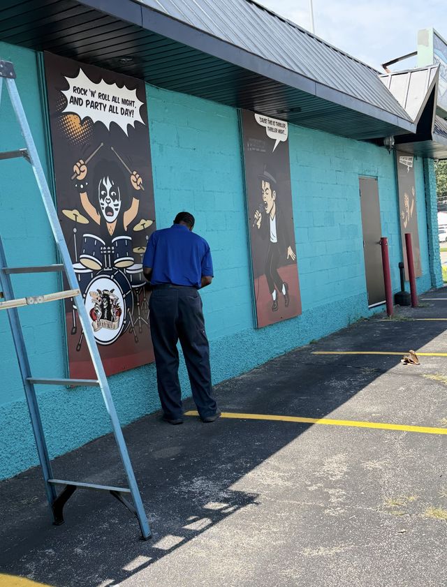 A man painting a mural on a teal building