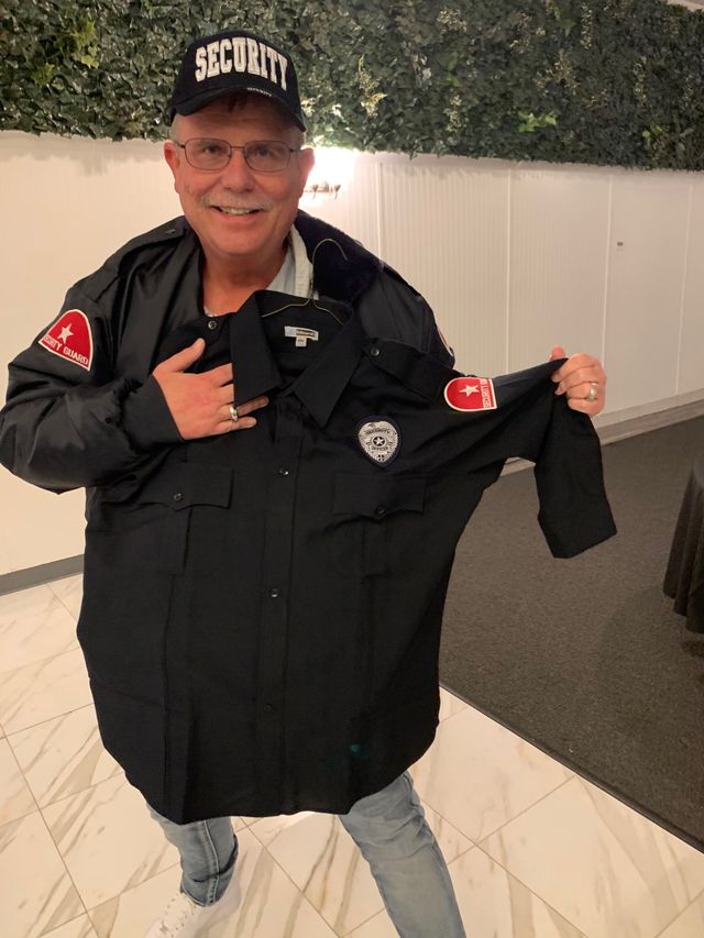 A man in a security cap and jacket holding up a shirt