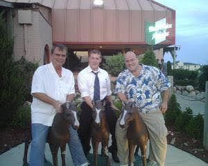 Three men posing with ponies outside a restaurant