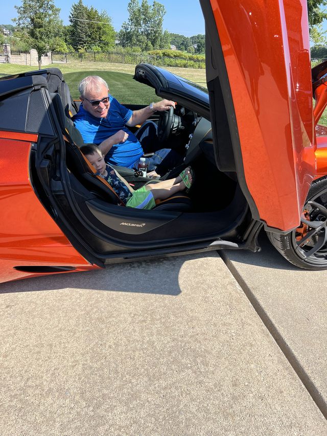 A man in the driver's seat of an orange McLaren with its door raised