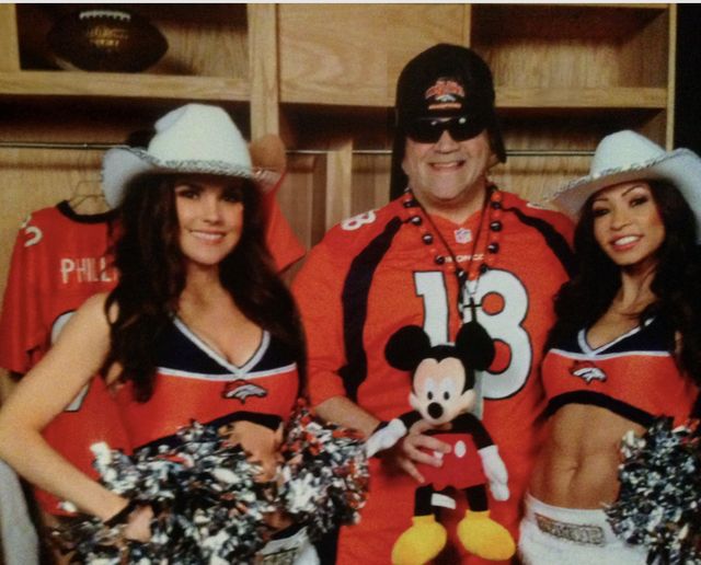 A man in a football jersey and mask with two cheerleaders