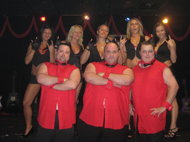 Three men in red shirts with a group of women on a stage