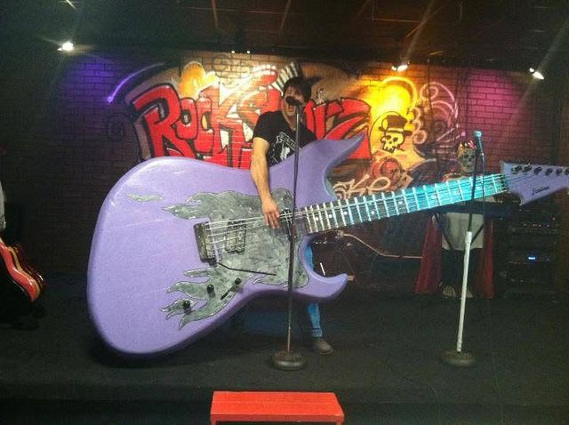 A man posing with a giant guitar sculpture